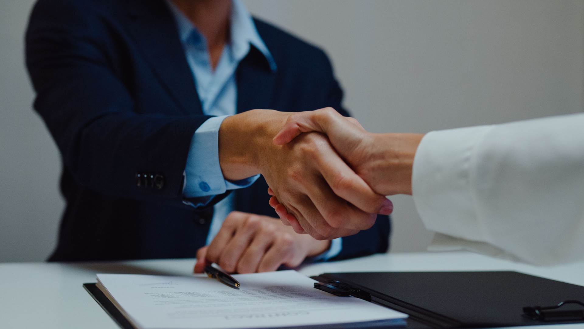 Closeup of young Asian businessman sign a contract investment professional document agreement and shake hands at office night. Businesspeople in workplace.