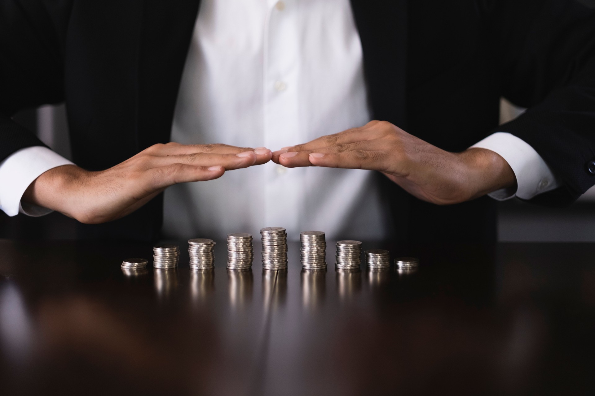 Businessman protecting increasing stacks of coins on desk